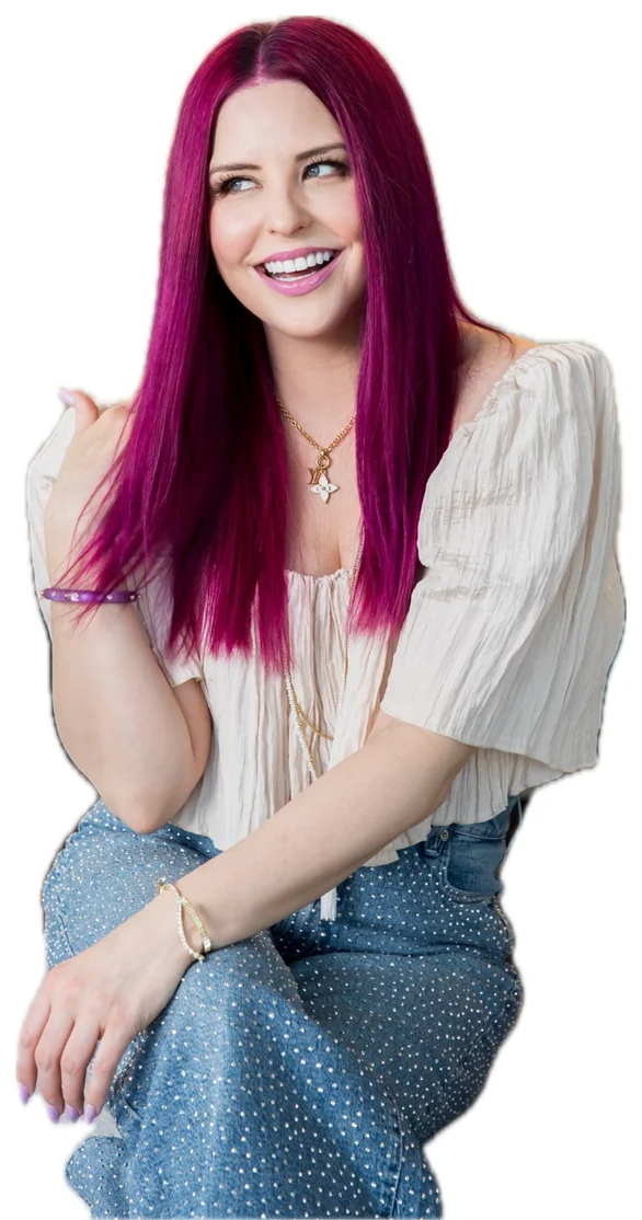 Ashley Diana smiling and pointing, in a cream top and sparkle jeans