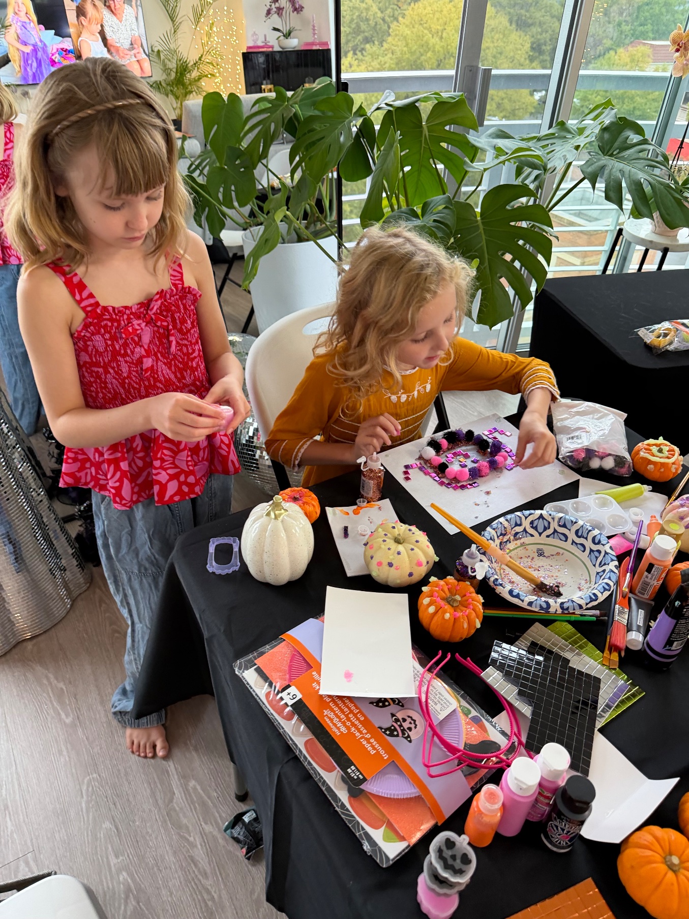 Lily and her friend decorating at the craft table with mini pumpkins, paints and pom-poms