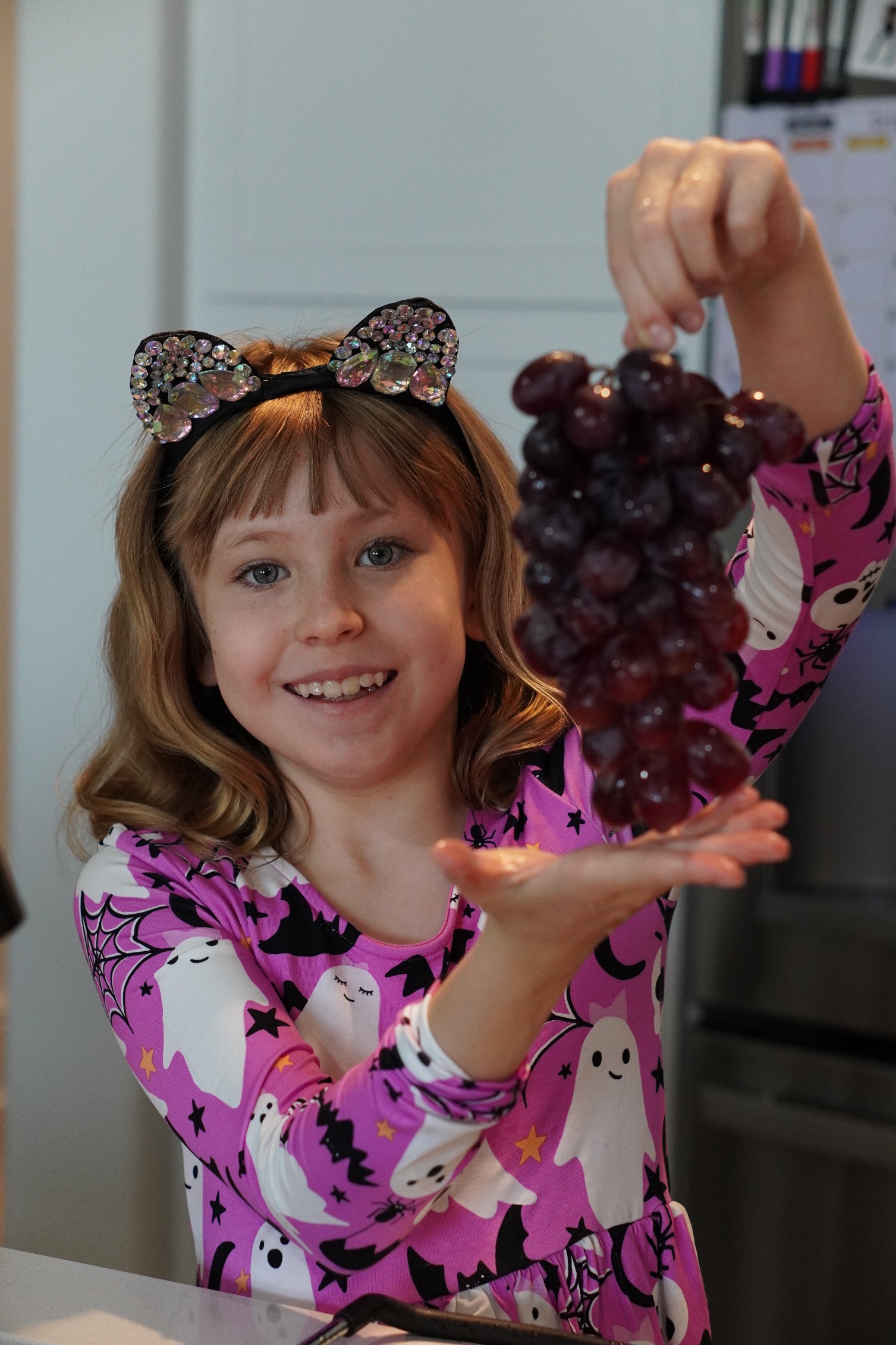 Lily holding a huge bunch of grapes at the Galloween party