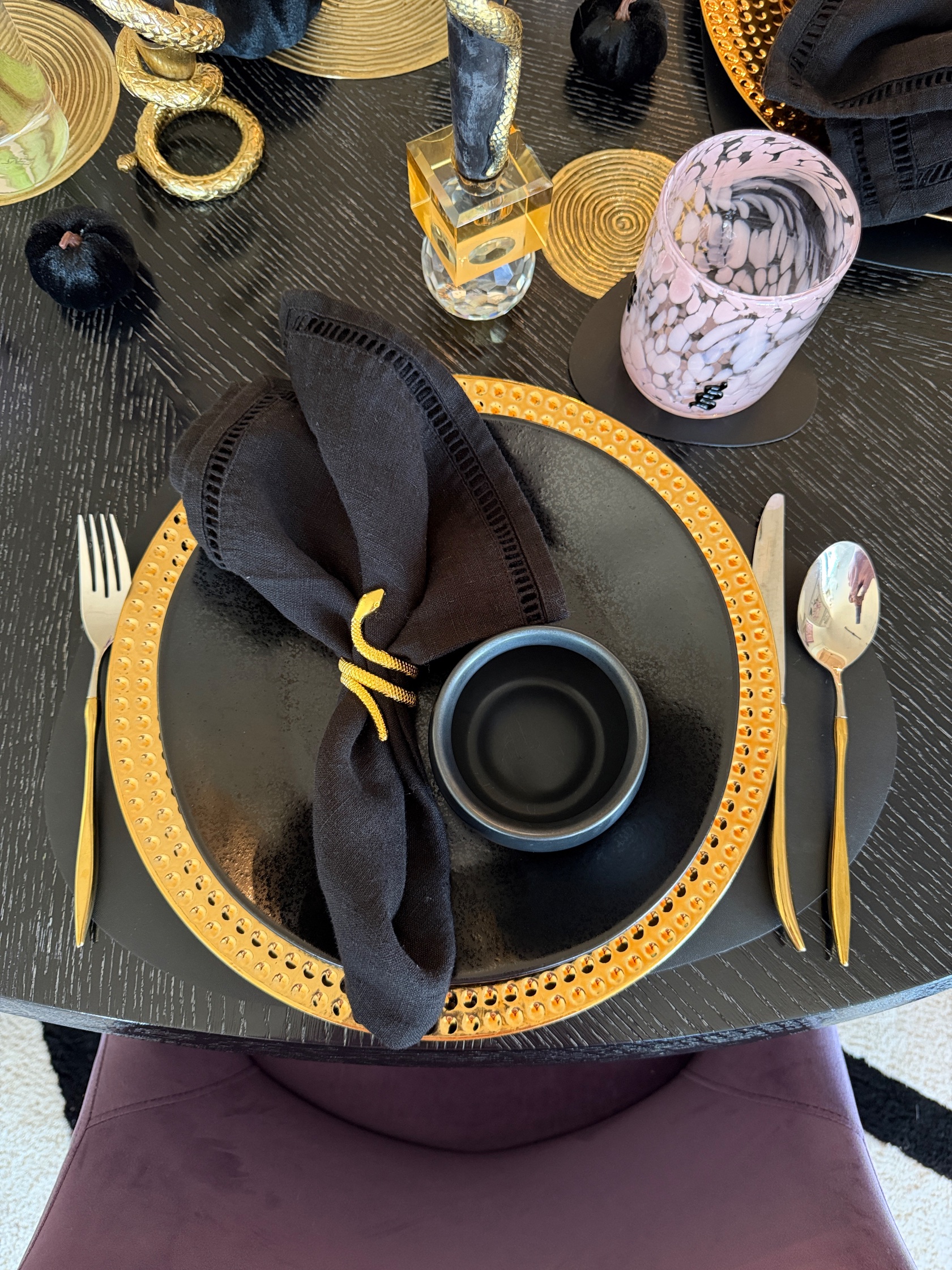 Galloween place setting with black dinnerware, a gold charger and a gold spider napkin ring
