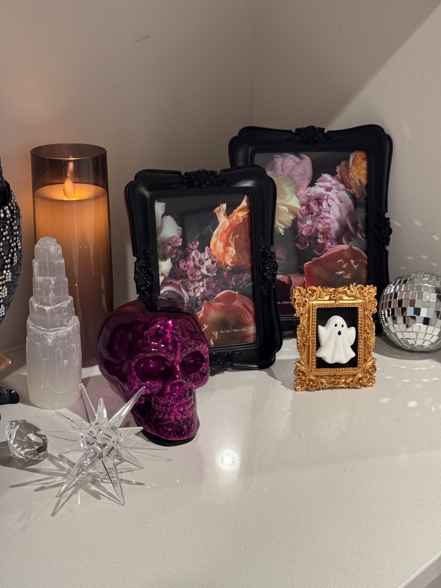Shelf vignette close-up with a magenta crackle skull, a ghost in a gold frame, floral art and a disco ball
