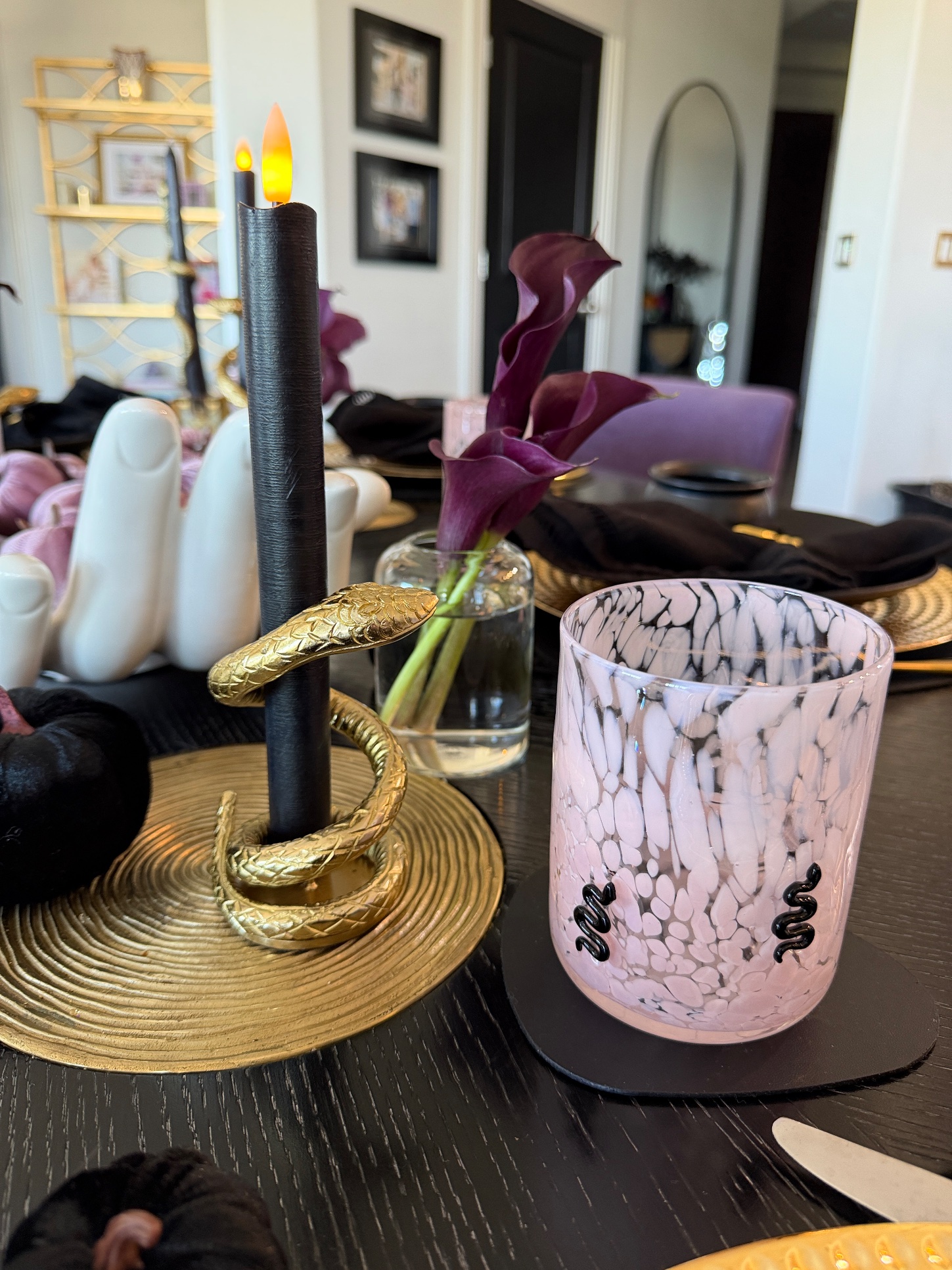 Close-up of a gold snake candle holder with a black taper, a calla lily and a pink marbled snake glass
