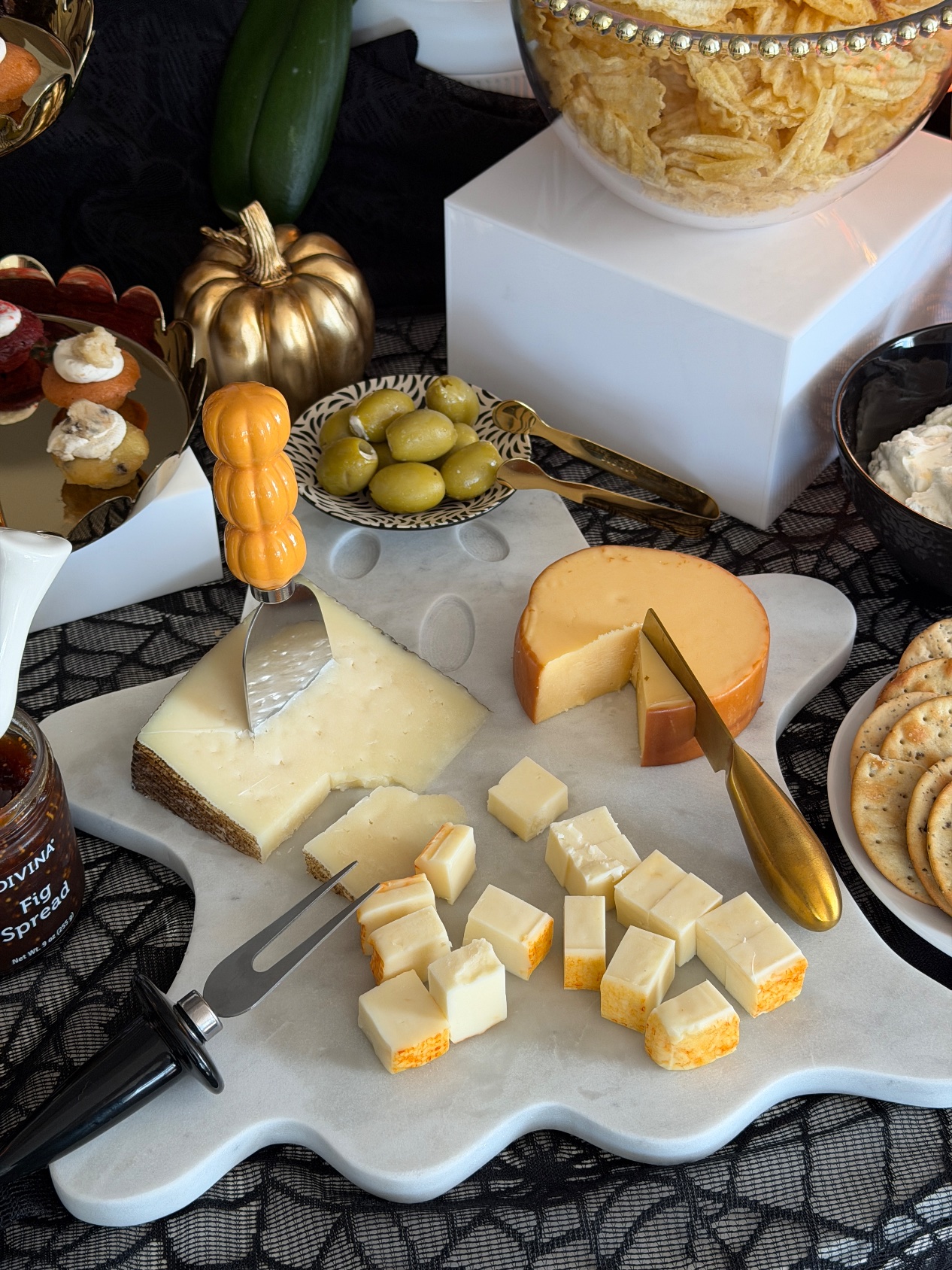 Cheese board close-up on the white ghost marble board with manchego, smoked gouda, green olives and Divina fig spread