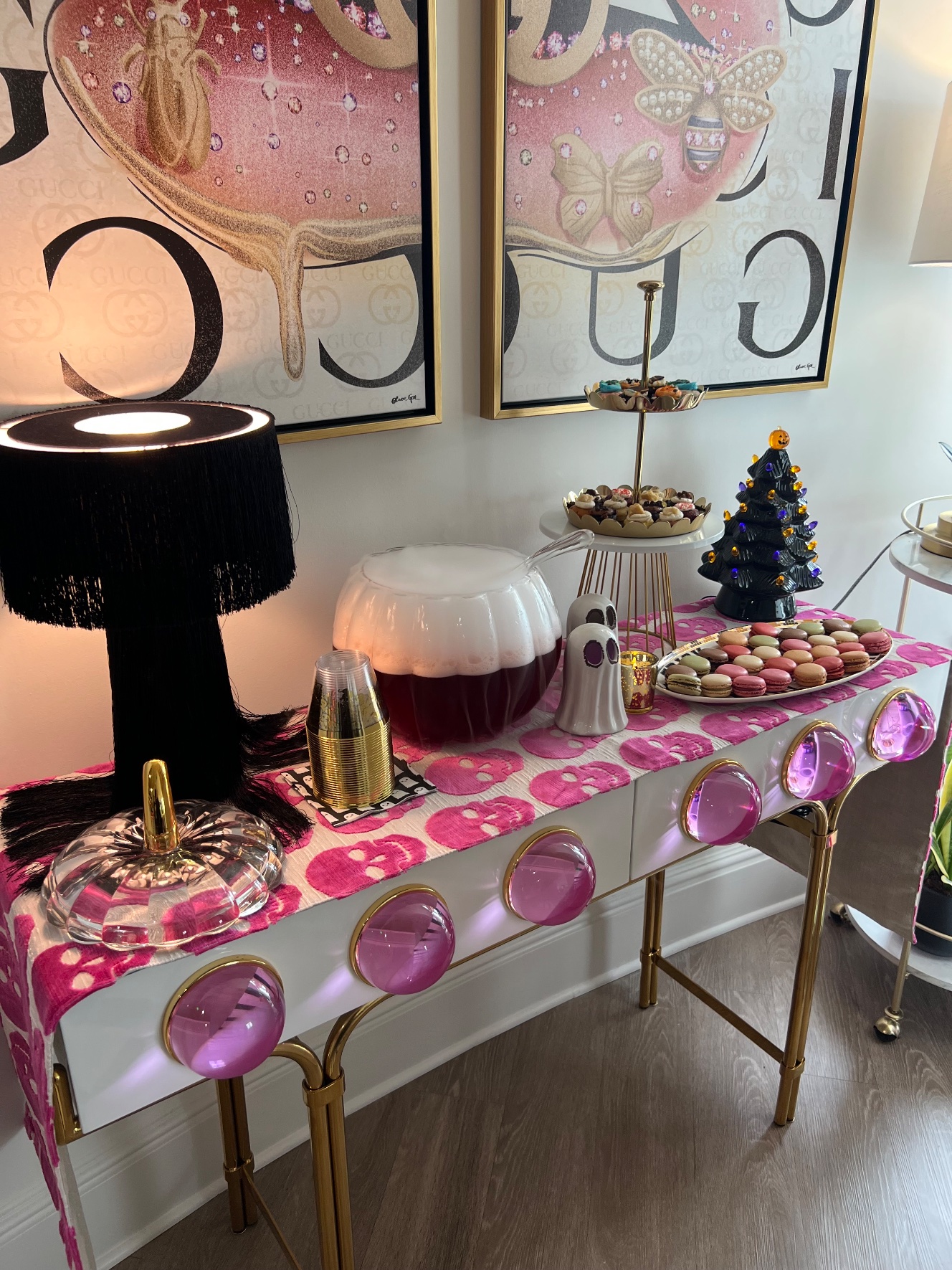 Drink and dessert station with a pink skull runner, smoking pumpkin punch bowl, tiered mini cupcakes and a plate of macarons