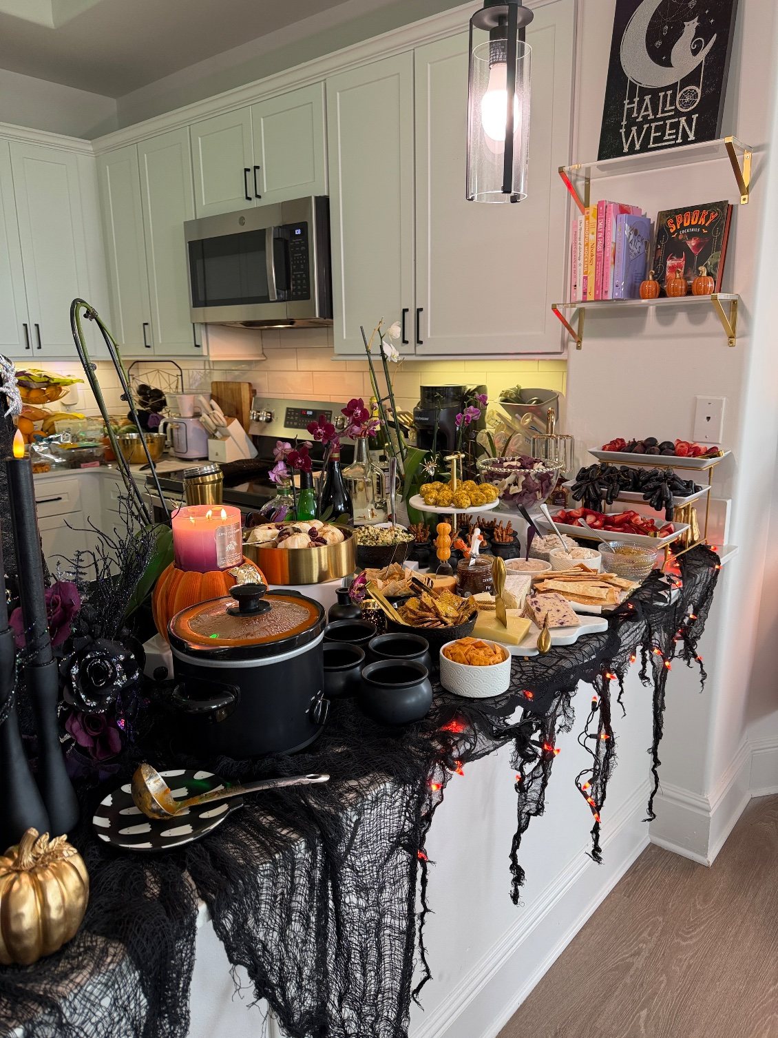 The whole Galloween grazing counter: slow cooker, black cauldrons, the cheese board, dips, ghost chips and the tiered fruit stand