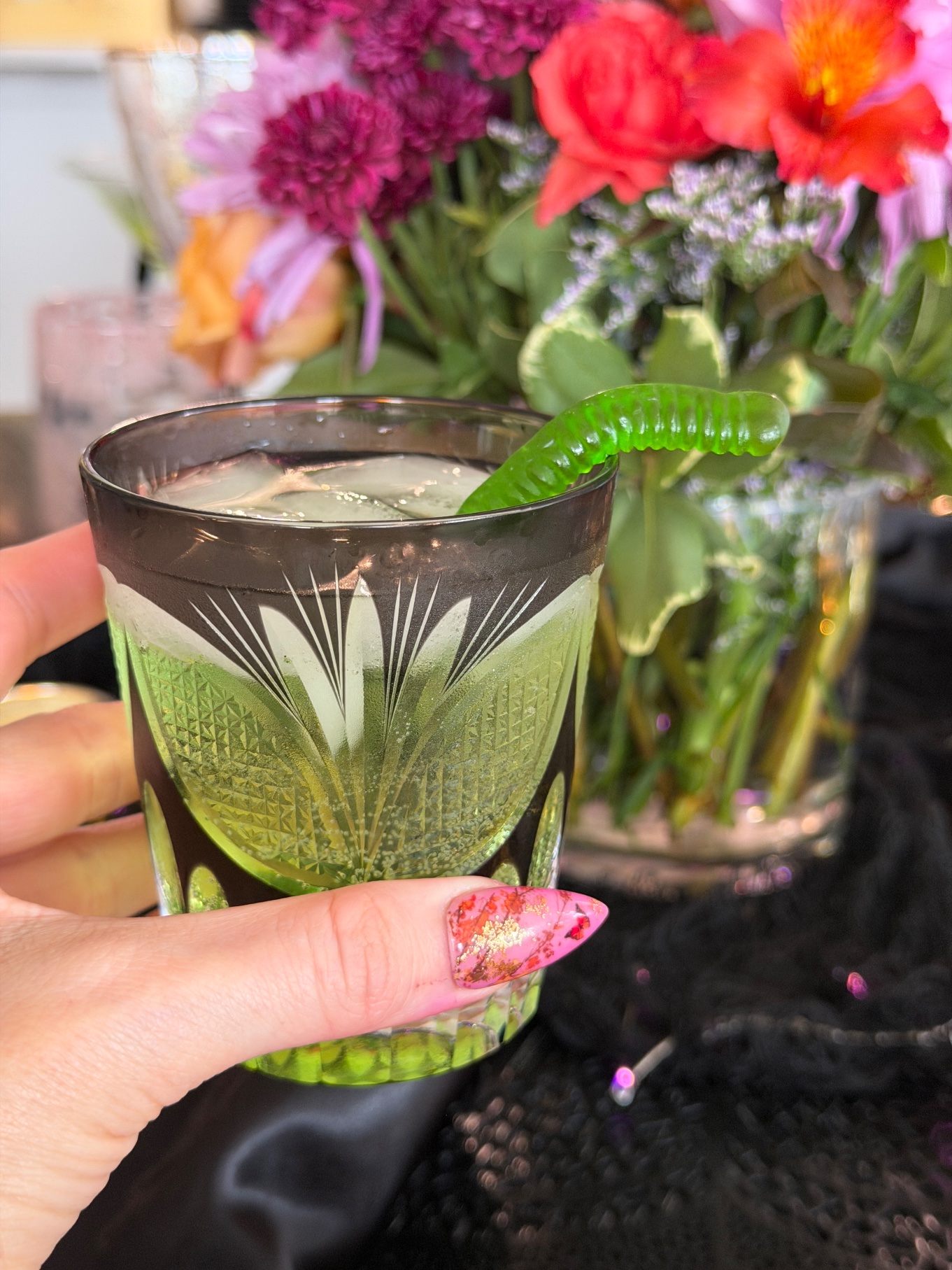 Green apple drink in a cut glass with a green gummy worm hanging off the rim