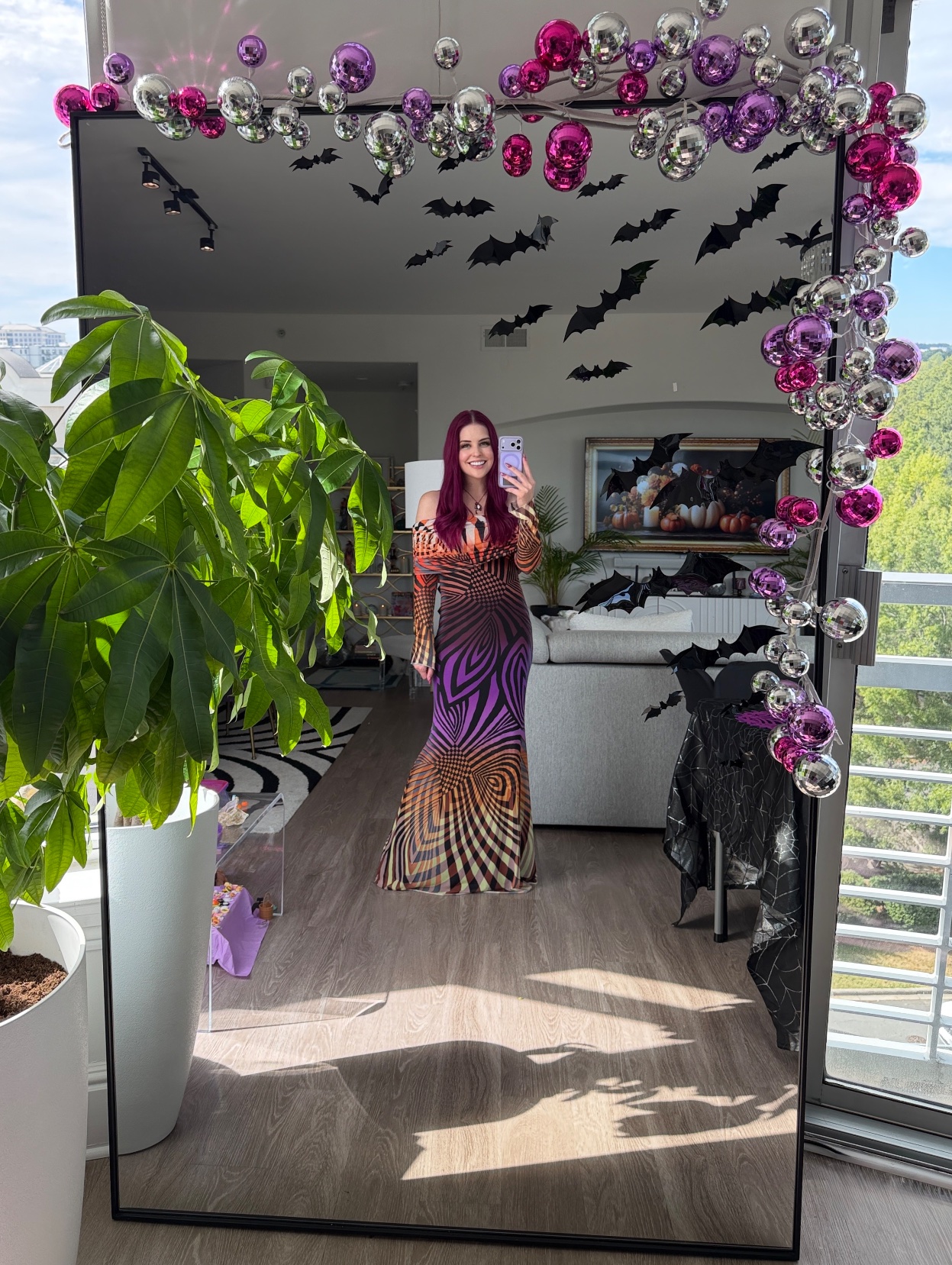 Ashley in her AFRM swirl print gown taking a selfie in front of the mirror framed with pink, purple and silver disco balls and black bats