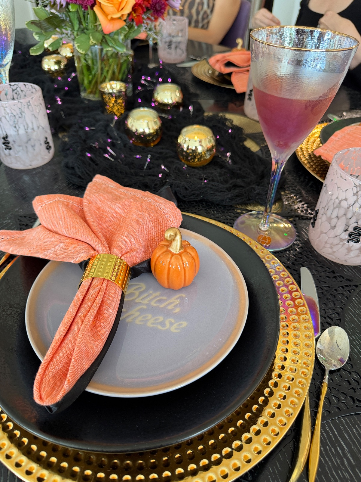 Place setting with a pink drink in an iridescent goblet and the floral centerpiece behind