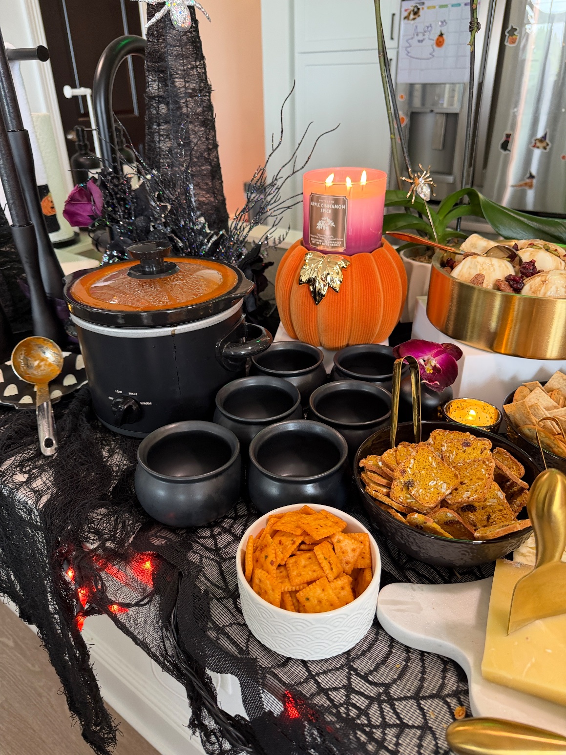 Slow cooker of Trader Joe's Autumnal Harvest Soup with mini cauldron bowls and a lit candle on a velvet pumpkin