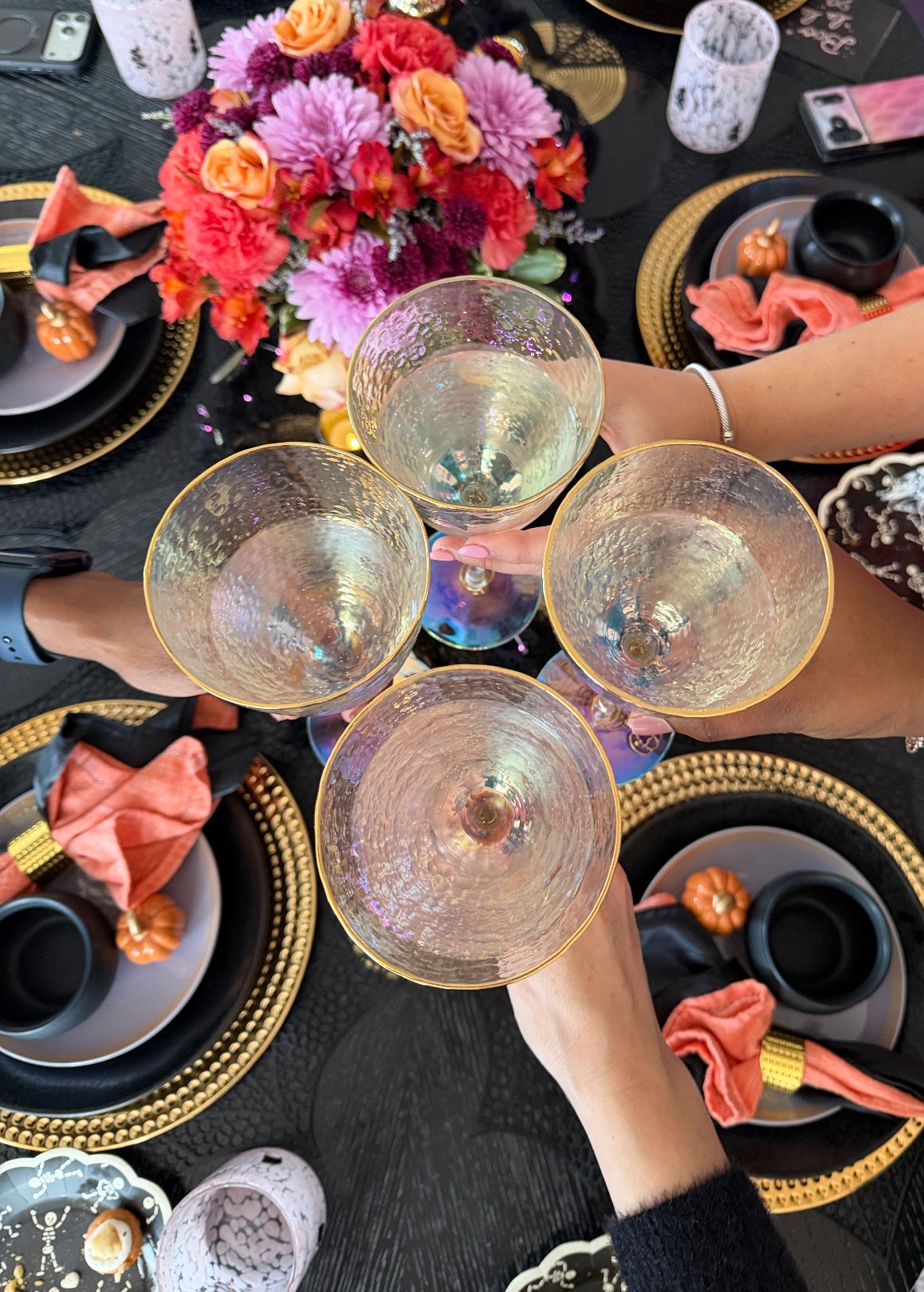 Four iridescent goblets with gold rims clinking in a toast over the Galloween table