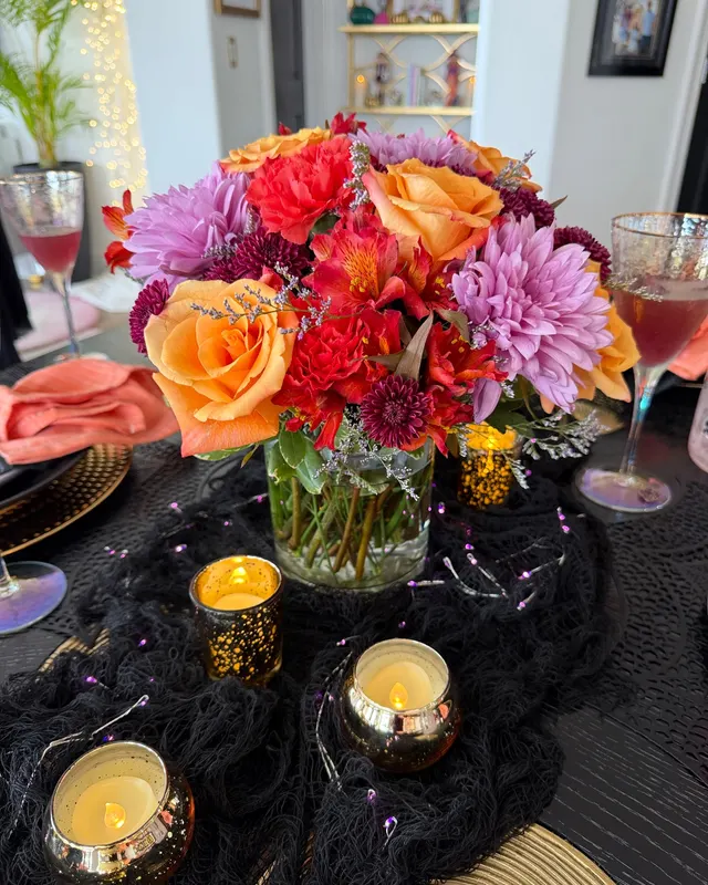 Galloween tablescape with a lush orange, red and lavender floral centerpiece, gold votives and purple fairy lights on a black gauze runner