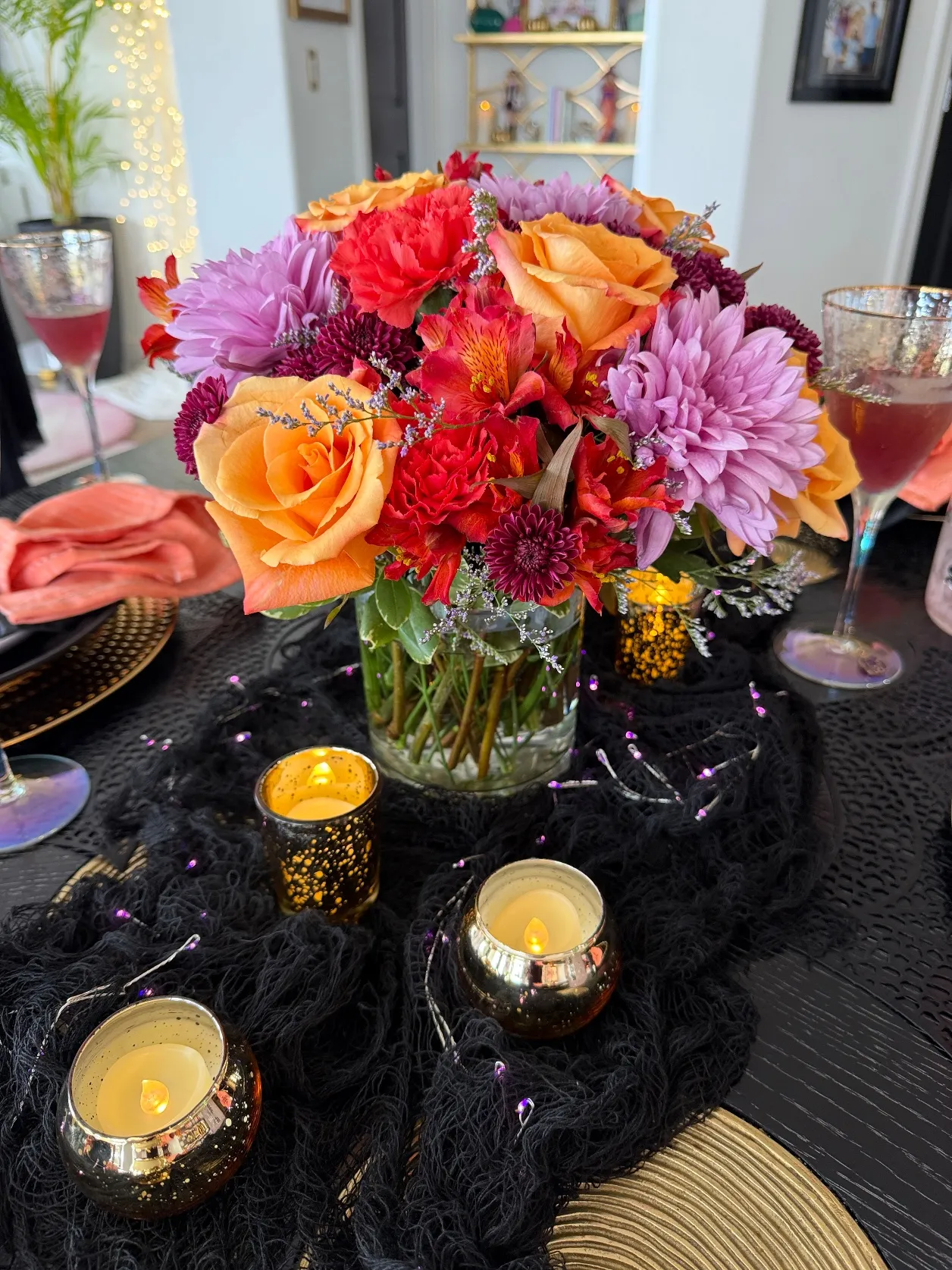 Galloween tablescape with a lush orange, red and lavender floral centerpiece, gold votives and purple fairy lights on a black gauze runner